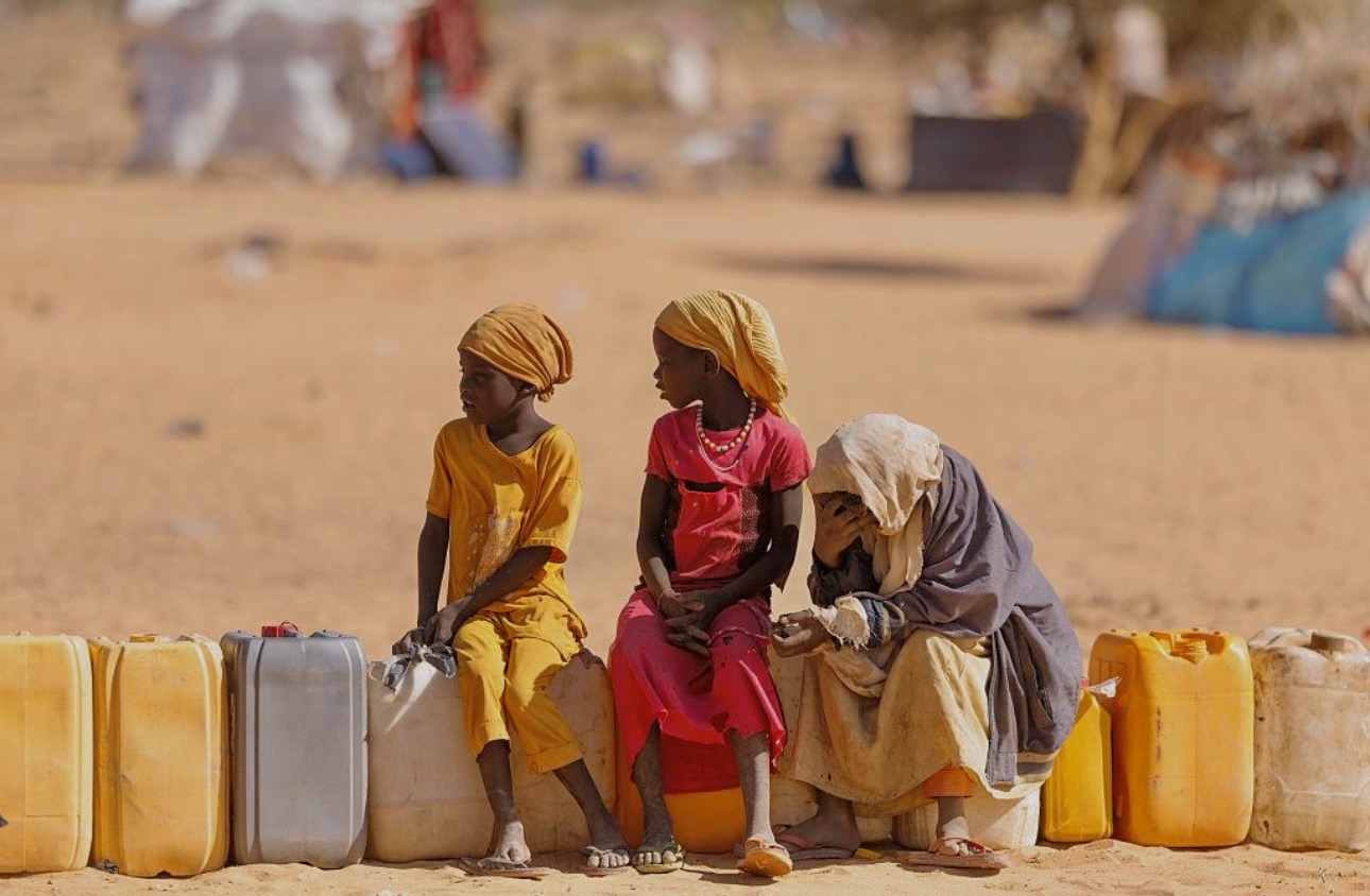 Des enfants assis près de bidons d’eau